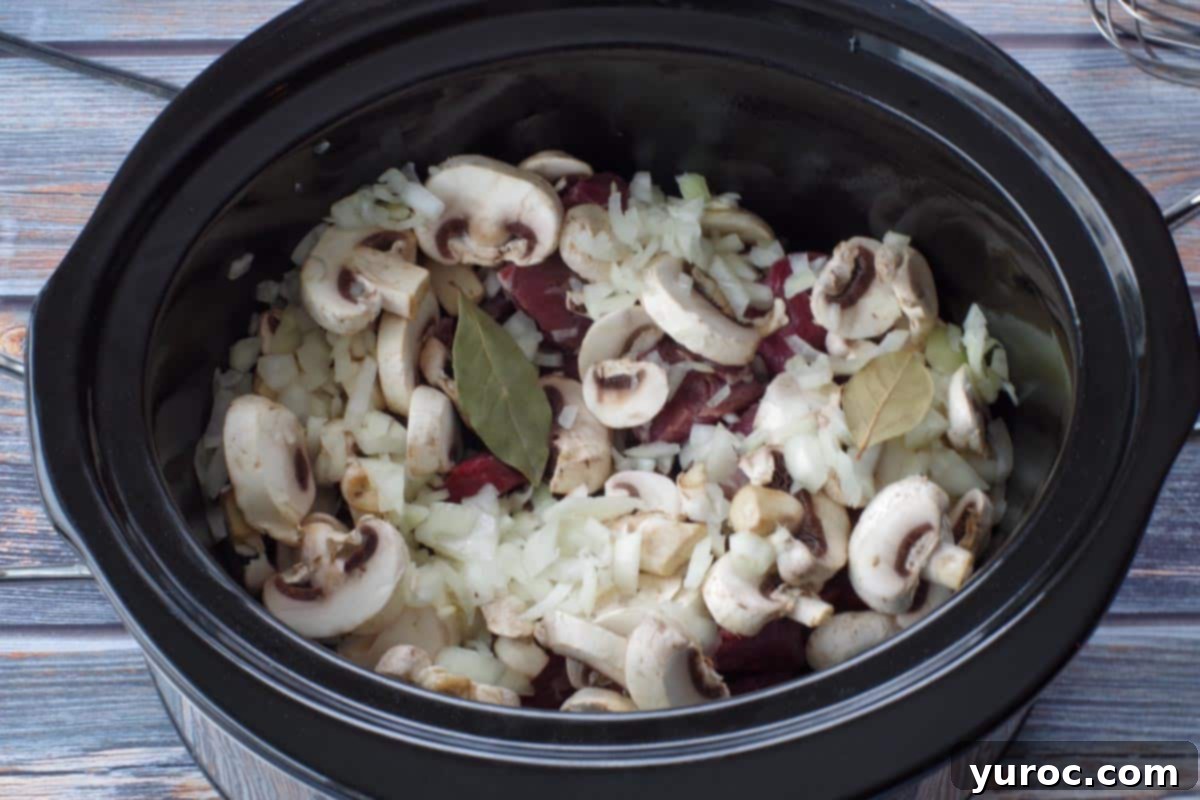 uncooked beef, mushrooms onions and bay leaves in a crockpot