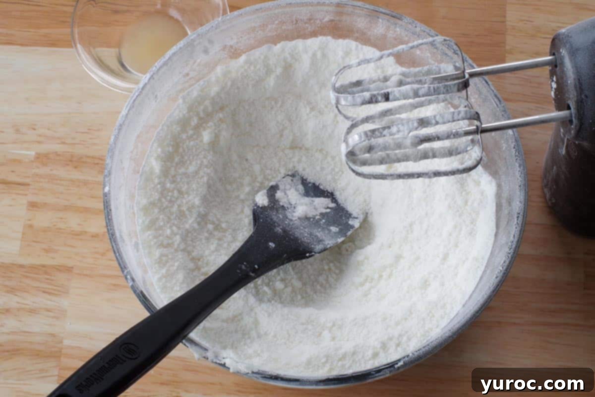 Vegetable shortening and powdered sugar mixed in a glass bowl with a black spatula.