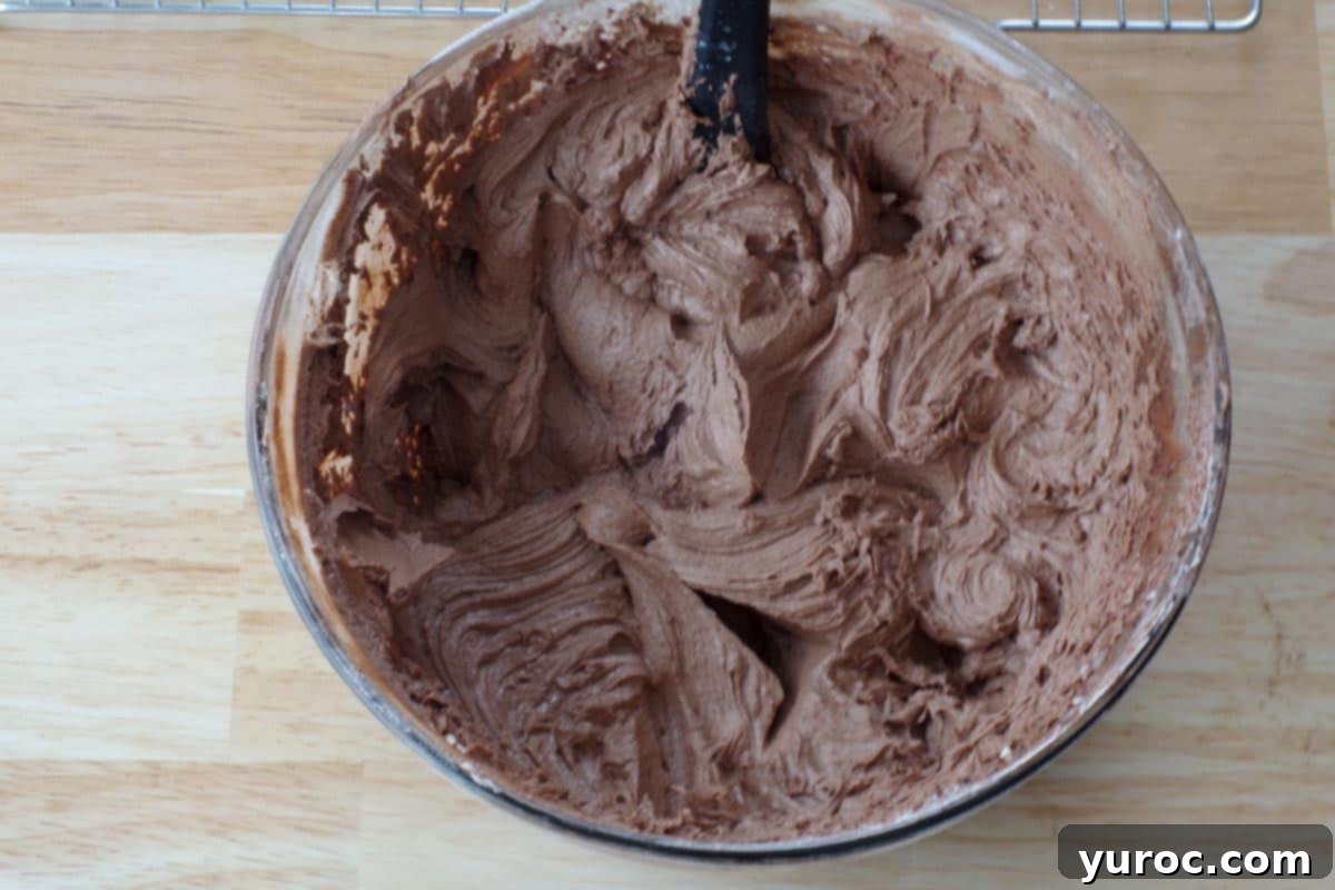Cocoa powder, vanilla extract, Irish cream, and milk being added to the shortening and powdered sugar mixture.