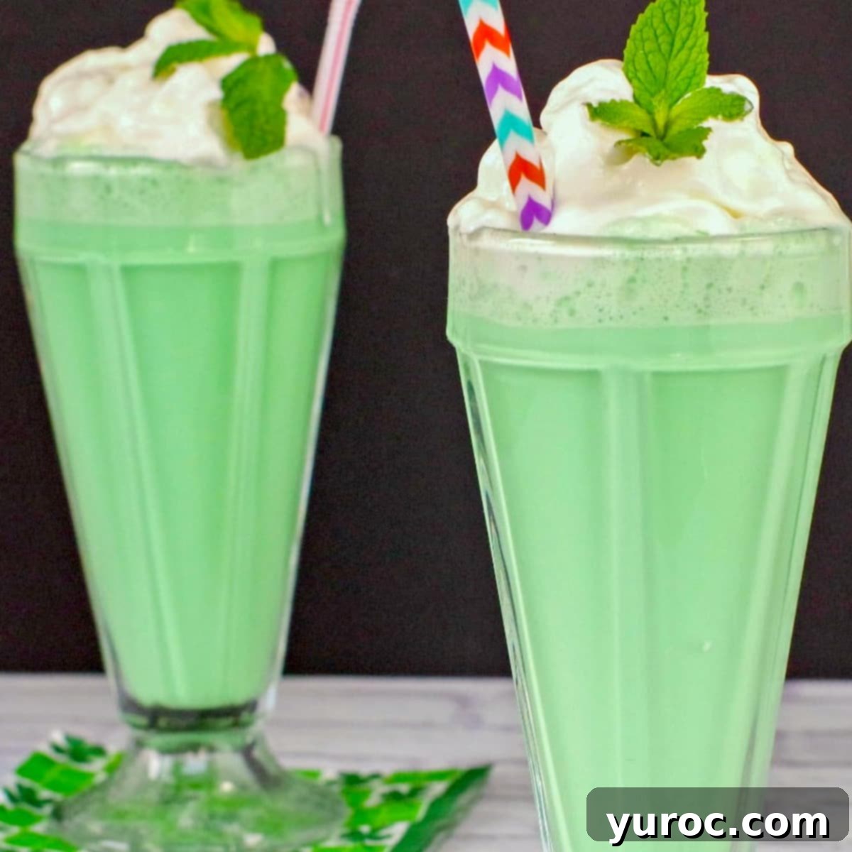 Two non-alcoholic Green Grasshopper mocktails garnished with mint, on a white surface with a dark background, complementing the cake.