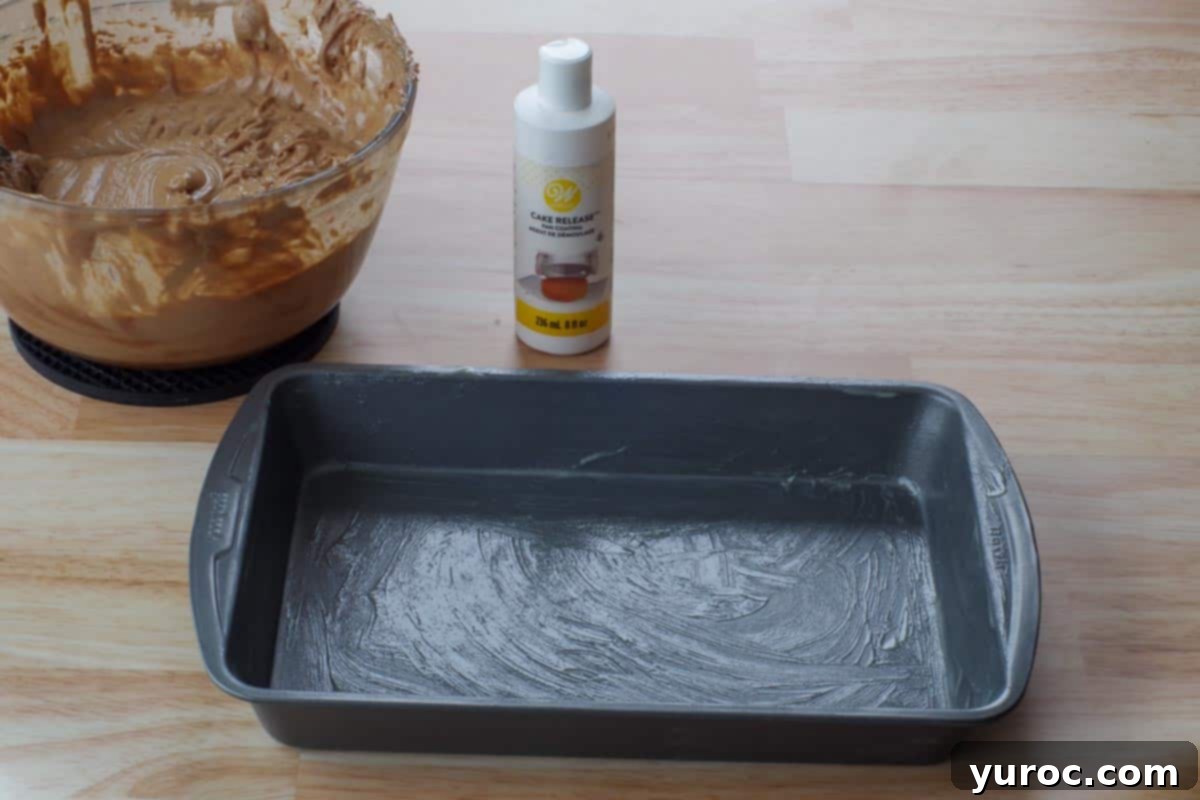 A greased 9x13 inch cake pan with a bottle of cake release, and the cake batter in the background.