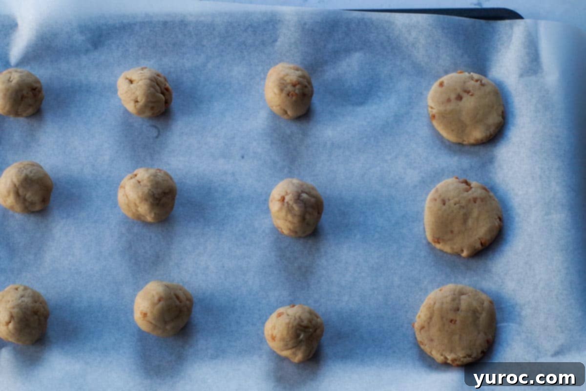 cookie dough rolled into balls on a parchment covered baking sheet, with some flattened