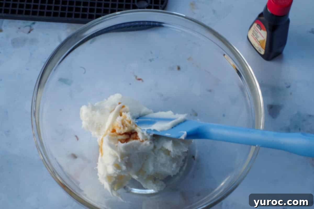 rum extract being mixed into frosting in a glass bowl, with a blue spatula