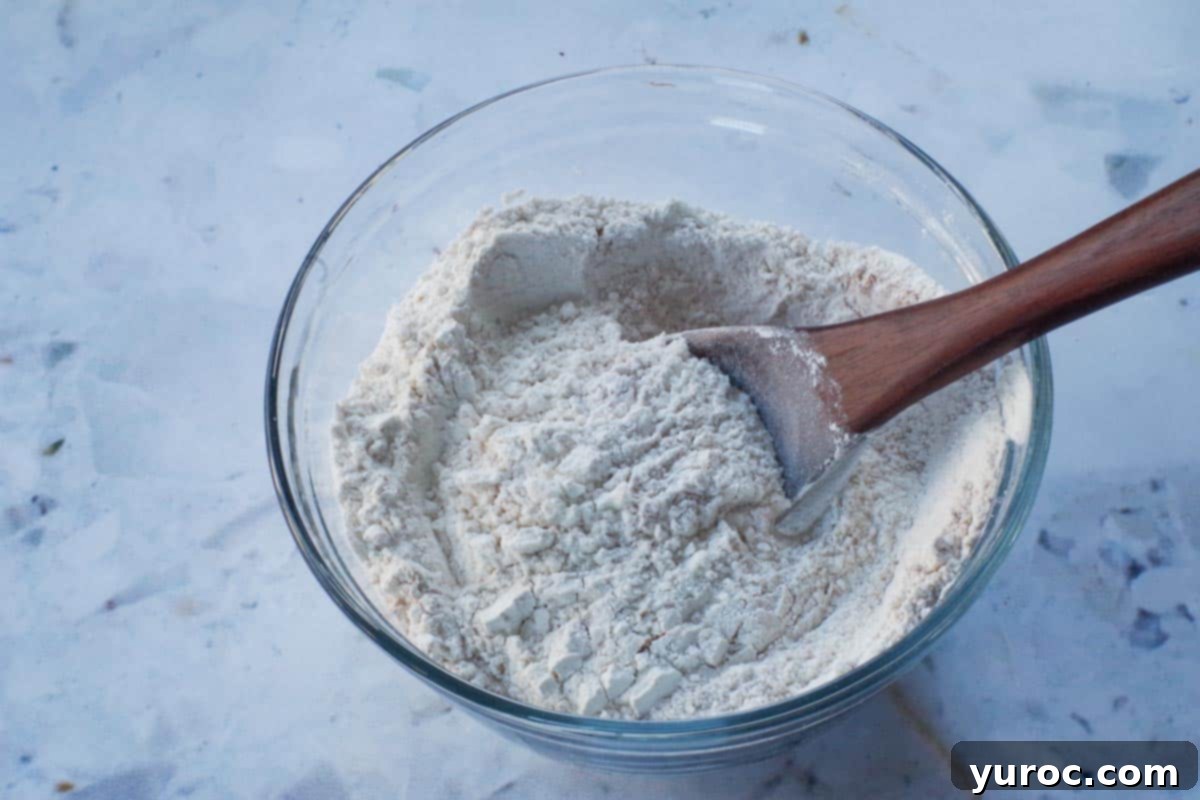 dry ingredients mixed together in a glass bowl with a dark wooden spoon