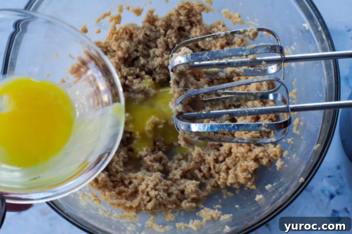 egg yolks being added to wet mixture in glass bowl, with beaters over top of bowl