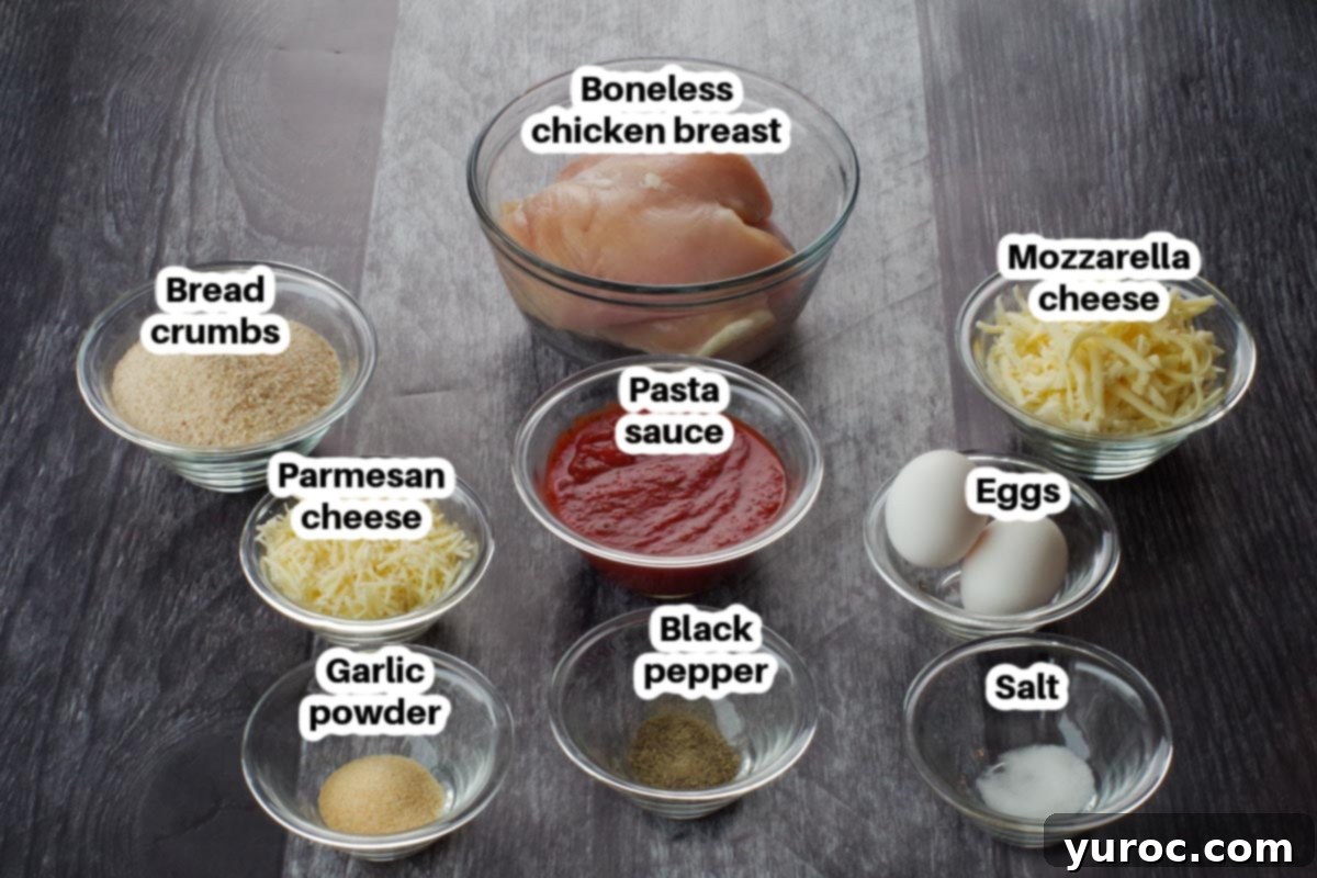 Ingredients for one-pan chicken parmesan laid out in glass bowls on a faux wood surface, including breadcrumbs, cheese, and spices.