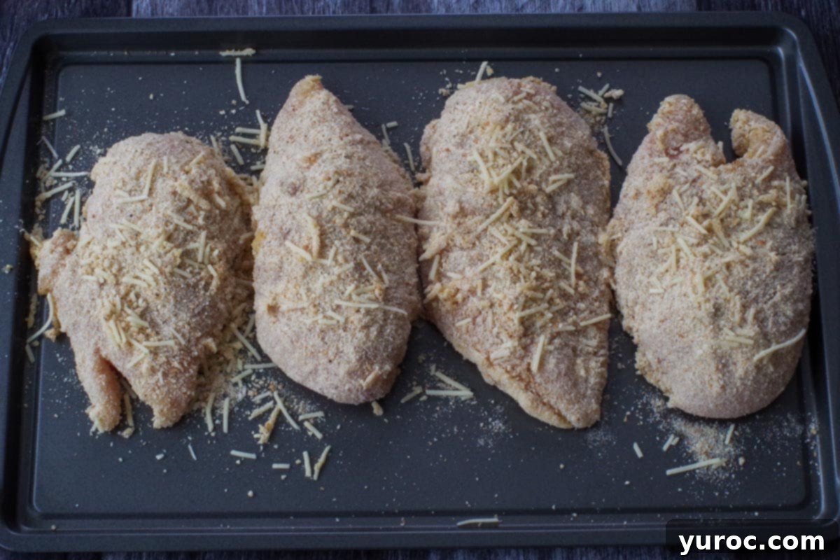 Four breaded chicken breasts arranged in a single layer on a prepared baking sheet.