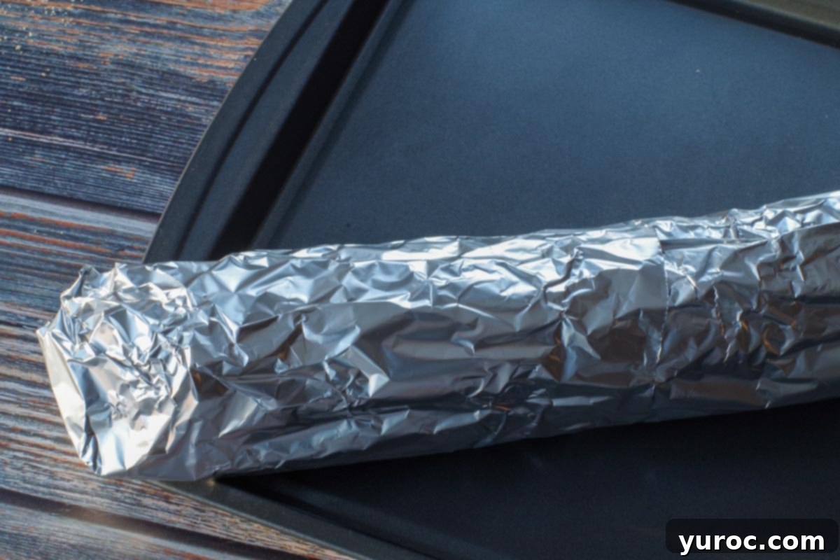 A close-up image showing a ripped section of aluminum foil around a baguette being repaired by wrapping an additional piece of foil over it, ensuring a secure seal.