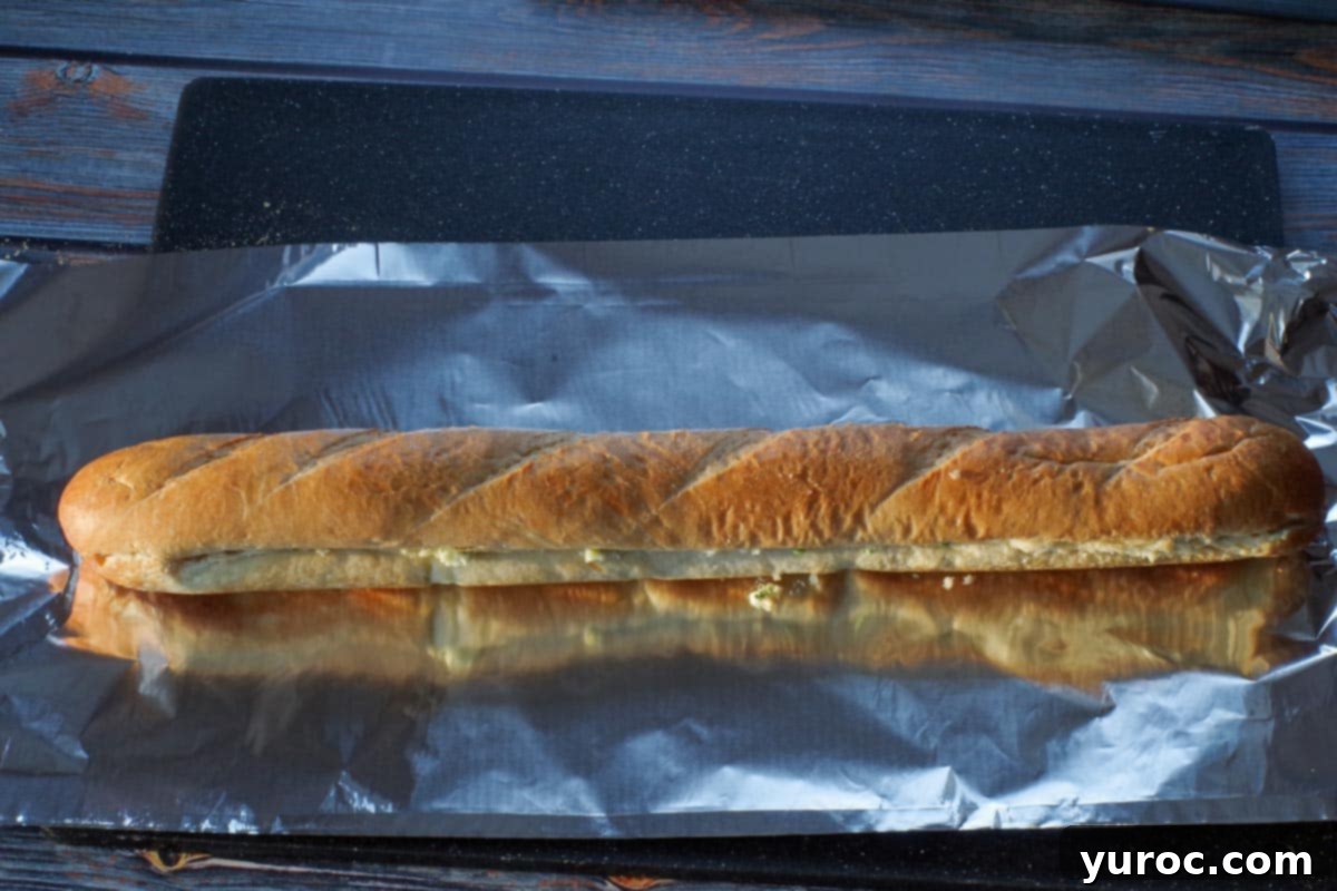 The two buttered halves of the baguette are reunited, and the entire loaf is placed on a long piece of aluminum foil, ready for wrapping.
