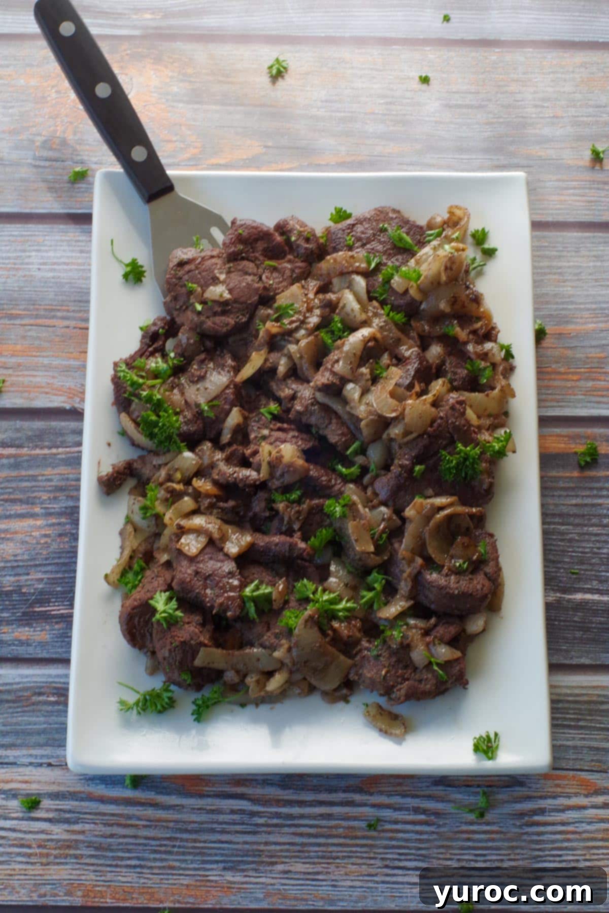 cooked venison steak on a white platter with a turner spatula, ready to be served family style