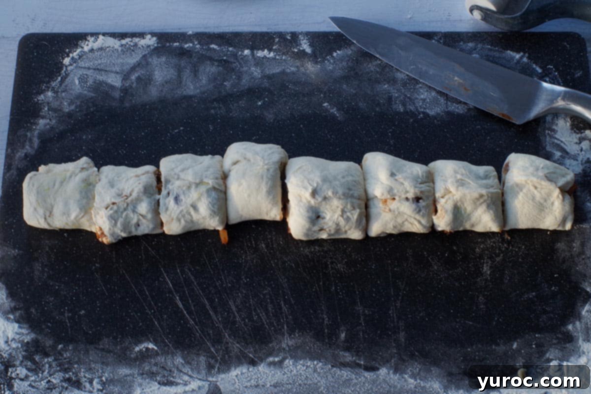 The rolled cinnamon roll dough log, expertly sliced into eight perfectly equal pieces, ready for baking.