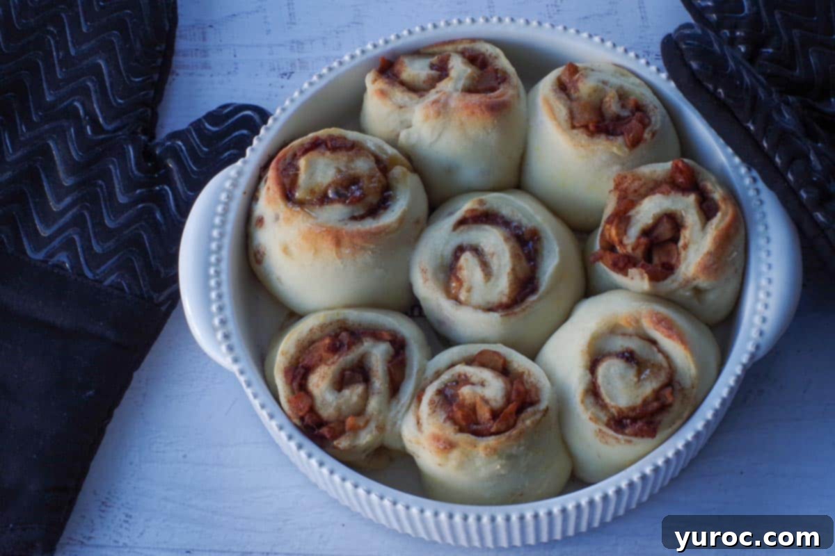 Apple pie 2-ingredient cinnamon rolls baking to a golden crisp in a white ceramic baking dish, filling the kitchen with a delightful aroma.