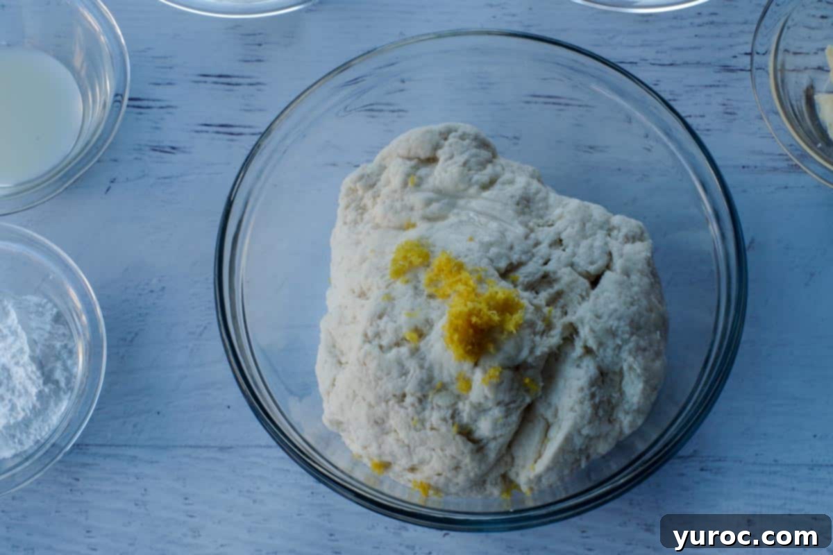 Lemon zest and butter extract being added to the prepared 2-ingredient dough in a clear glass mixing bowl.