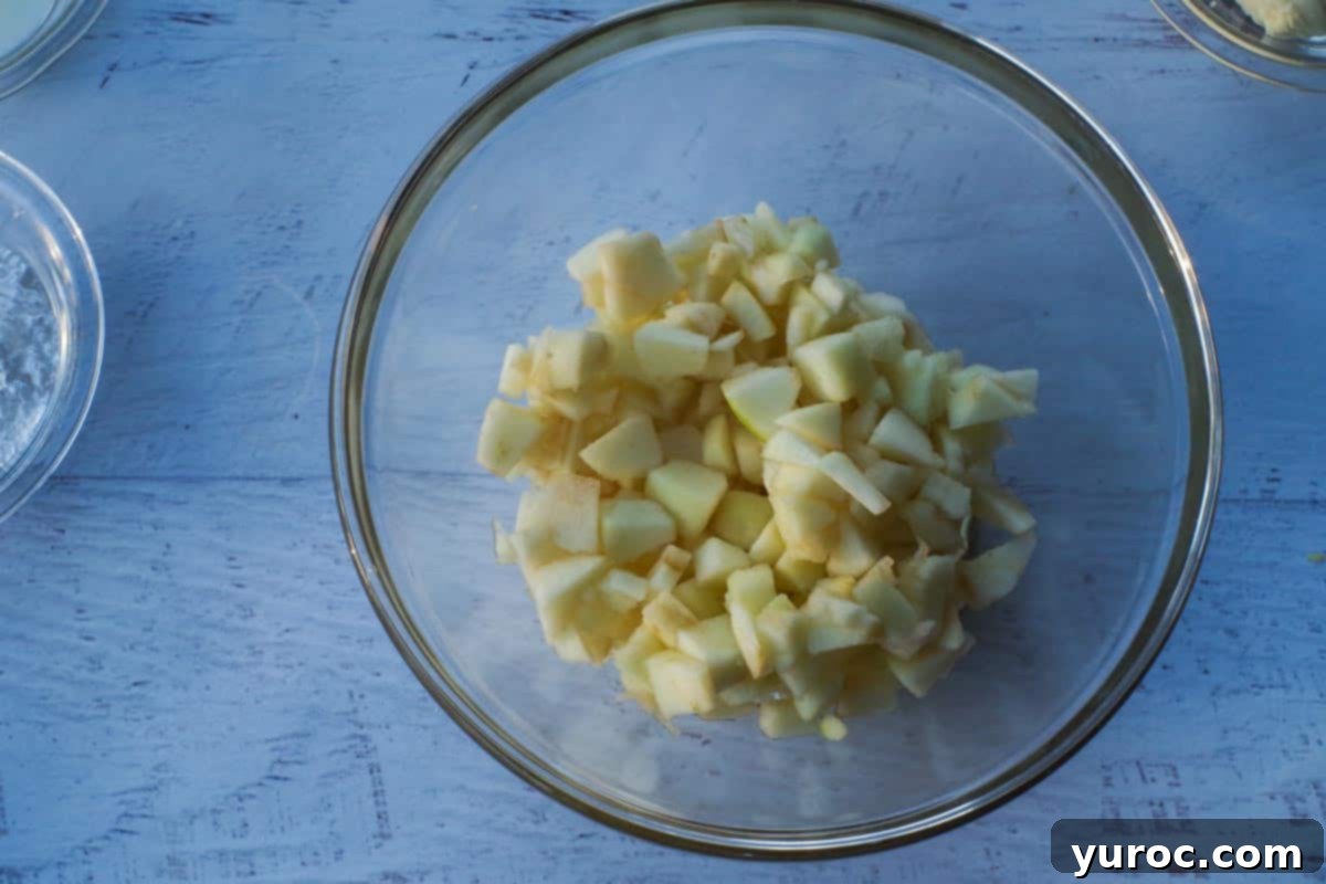 Neatly diced fresh apples in a transparent glass bowl, ready for cooking.