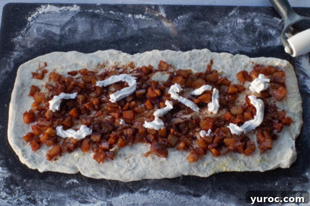 The spiced apple mixture spread across the buttered dough, with dots of light whipped cream sprayed on top.