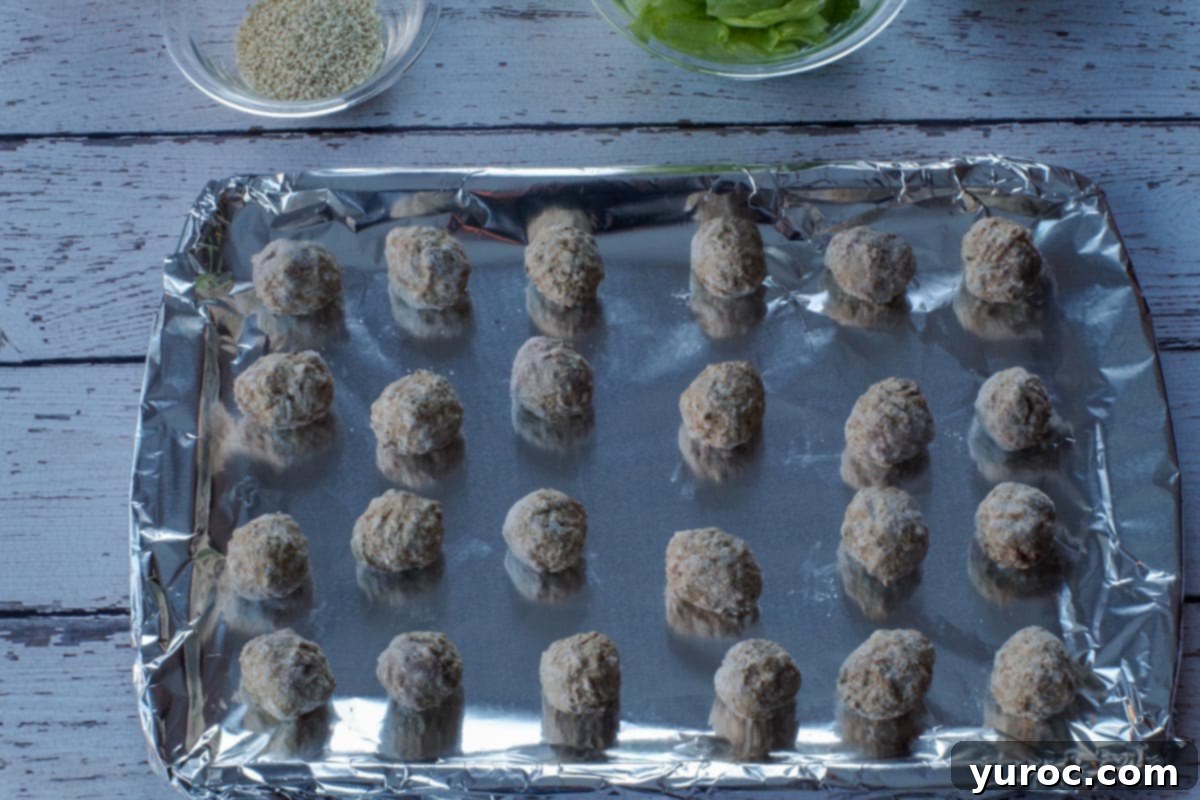 Frozen meatballs arranged evenly on a foil-lined baking sheet, ready for baking.
