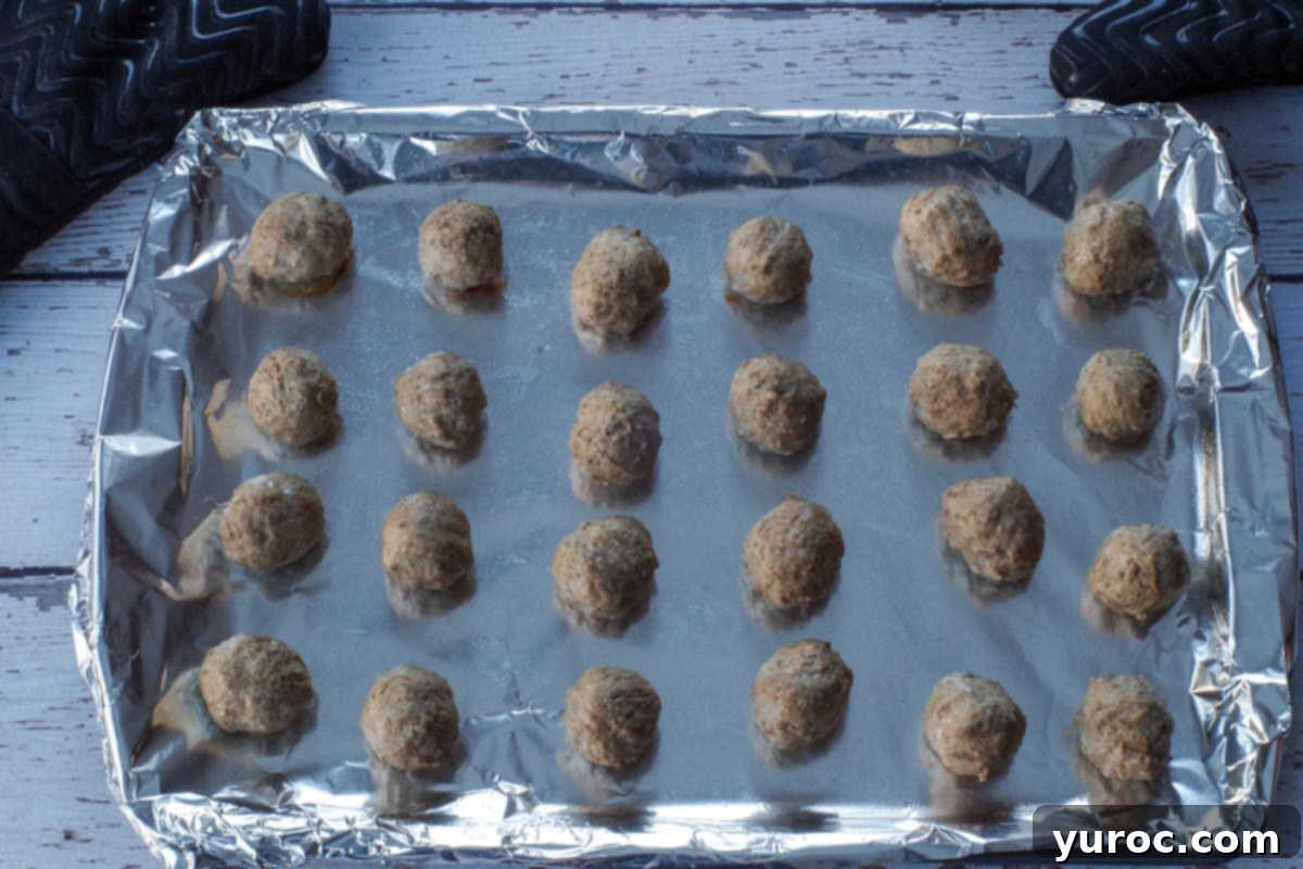 Cooked meatballs, browned and heated through, remain on the foil-lined baking sheet.