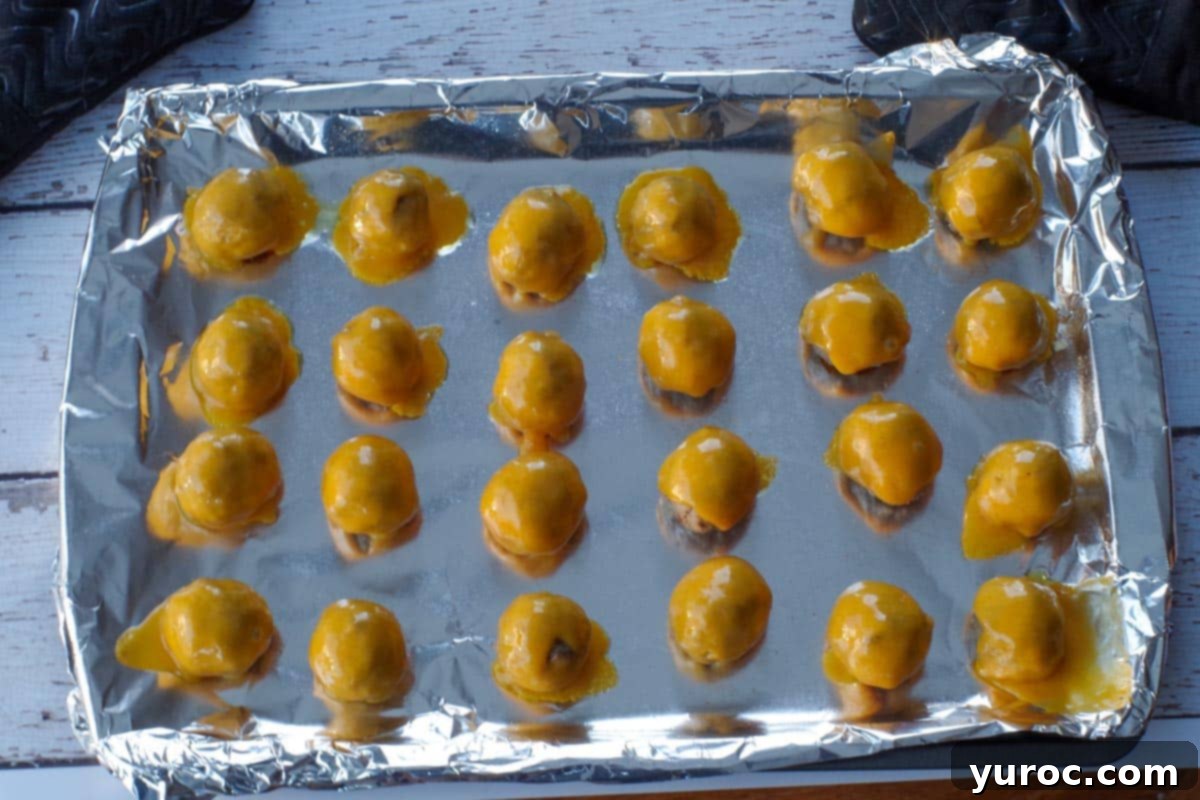 Close-up of cooked meatballs with perfectly melted cheddar cheese on top, ready for assembly onto skewers.