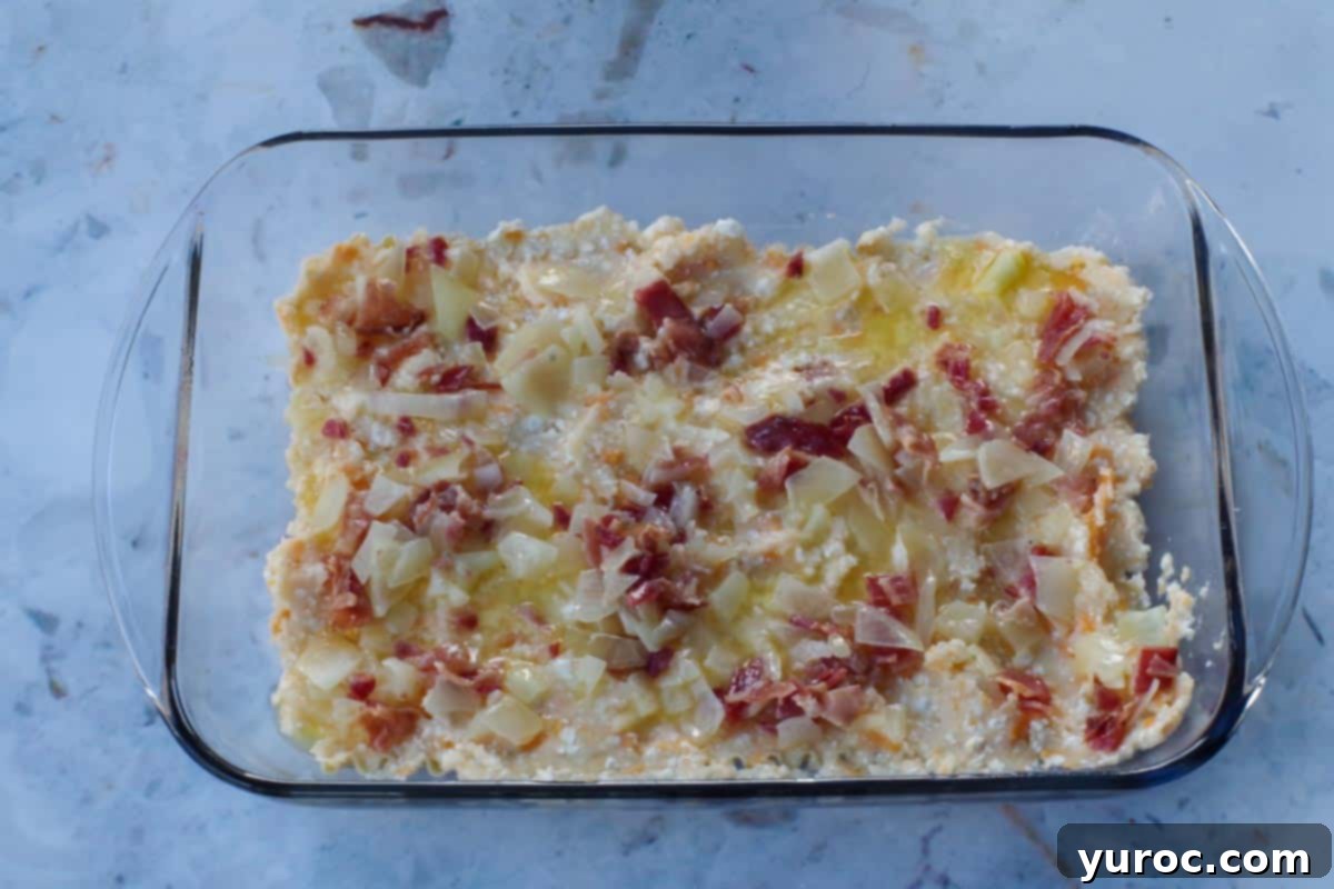 Easy Weeknight Pierogi Casserole 11 onion butter and bacon mixture spread over potato layer in glass pan
