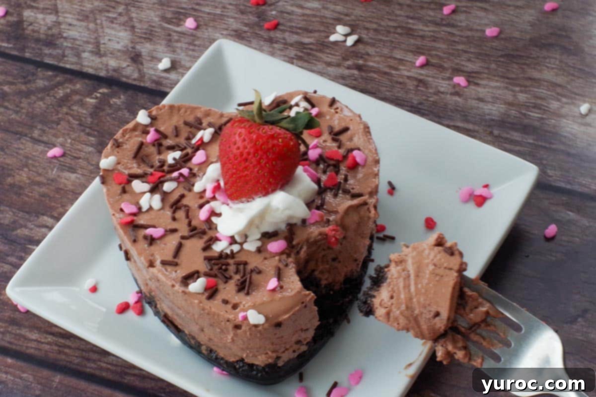 A heart-shaped Valentine's Day strawberry chocolate cheesecake displayed on a white plate, with a perfectly sized bite-sized piece held on a fork, ready to be enjoyed.