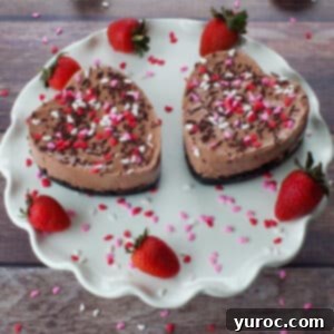 2 Valentine's Day Chocolate Strawberry Cheesecakes on a white cake platter with strawberries and heart sprinkles