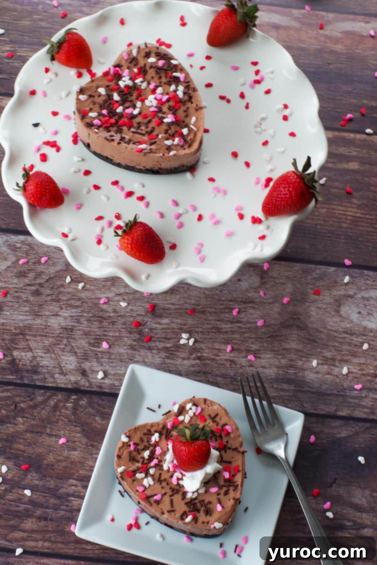 A beautifully presented heart-shaped Valentine's Day cheesecake on a white plate, with another cheesecake visible on a platter in the background, ready for a romantic celebration.