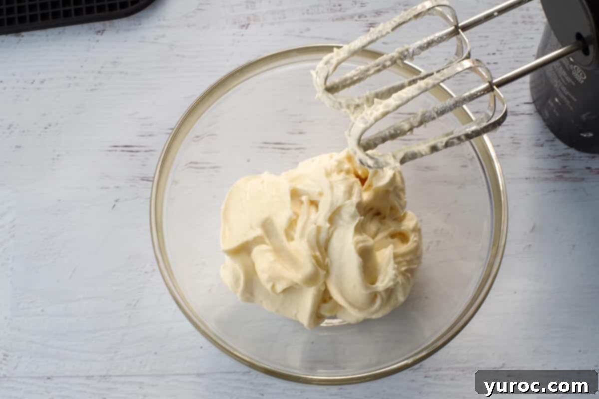 A bowl of creamy, sweet cream cheese butter, perfectly whipped and ready to be spread, with electric mixer beaters resting over the bowl.