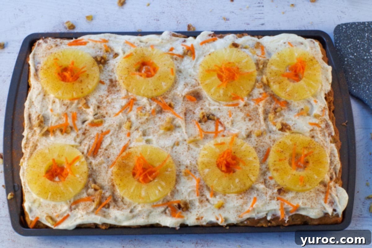 A close-up of sheet pan carrot cake pancakes, beautifully garnished with fresh pineapple, a dusting of cinnamon, grated carrot, and chopped walnuts, showcasing their delightful presentation.