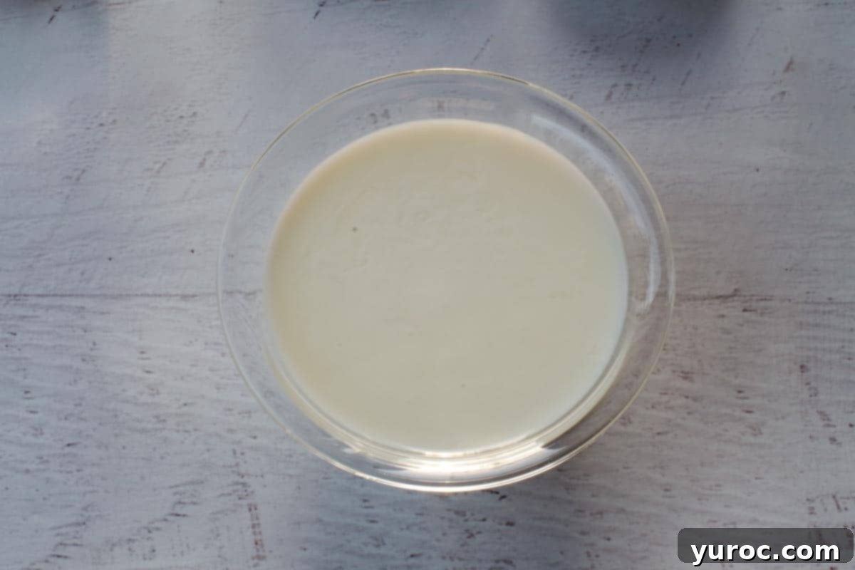Vinegar being gently poured into a bowl of milk, initiating the buttermilk substitute reaction, shown in a small glass bowl.