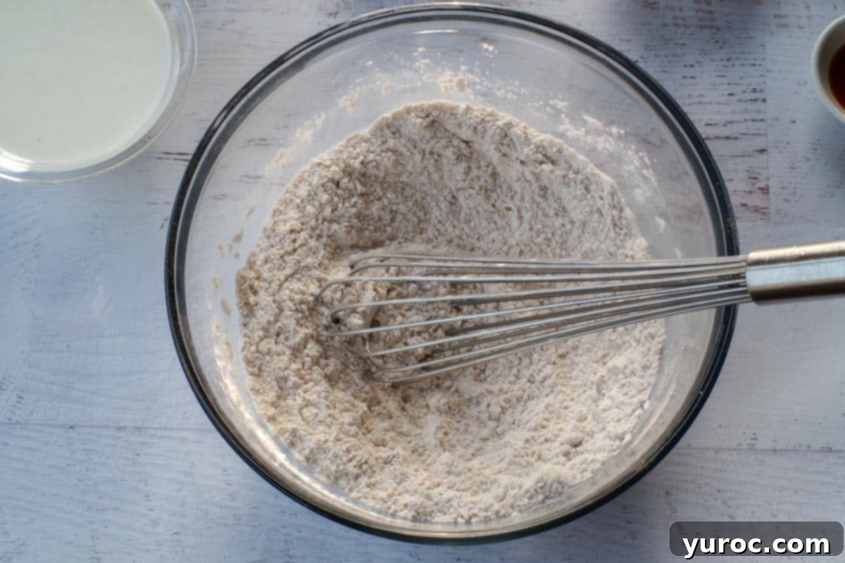 Dry ingredients, including flour, brown sugar, baking powder, baking soda, cinnamon, and nutmeg, are whisked together in a large mixing bowl to ensure even distribution.