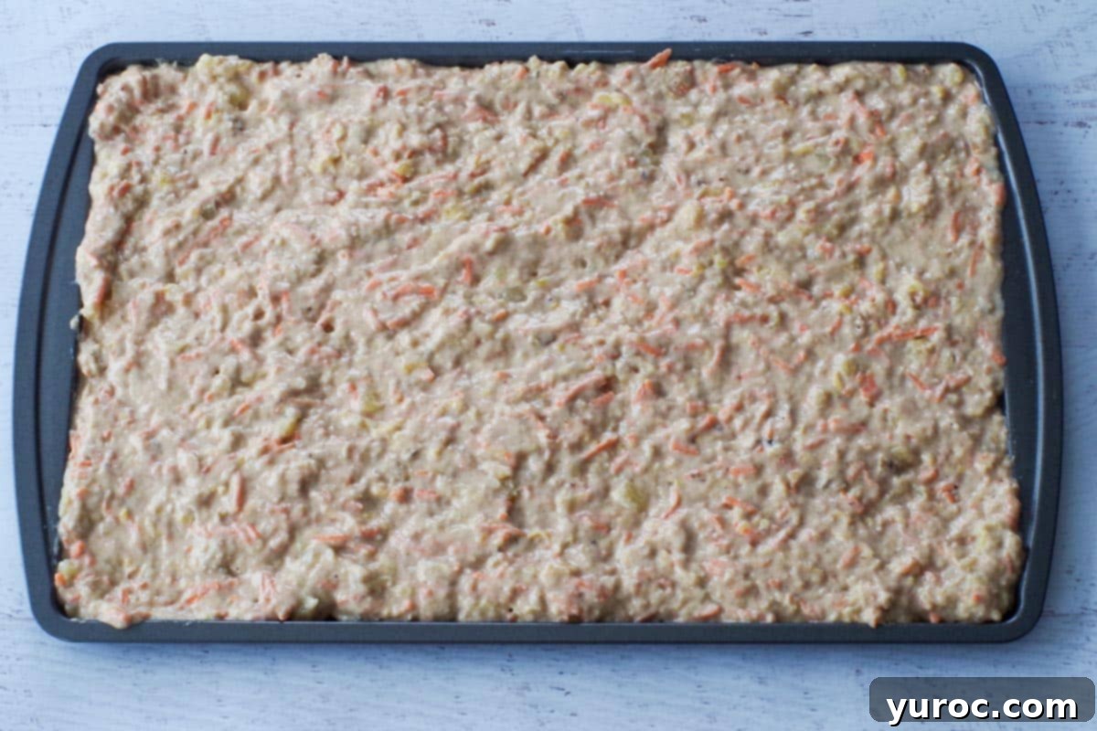 Smooth, evenly spread pancake batter covering the entire surface of a prepared baking sheet, ready for the oven.