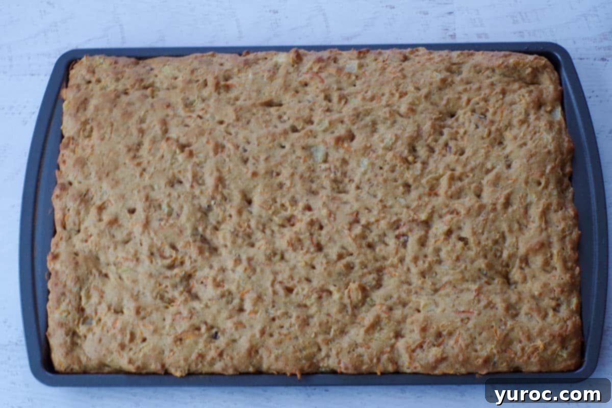 A freshly baked, golden-brown carrot cake pancake sheet sitting in a 9x13 inch sheet pan, cooled and ready for frosting.