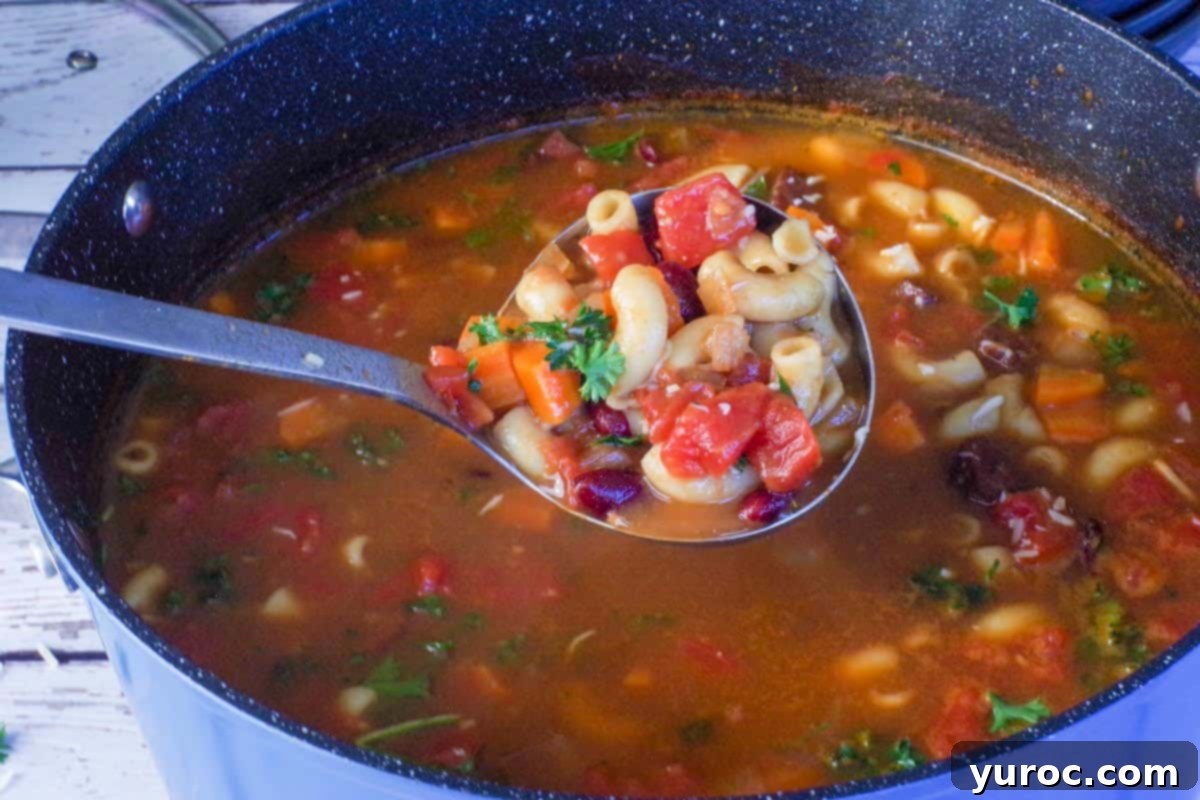 Hearty Ham and Macaroni Soup 8 A ladle lifts a generous portion of steaming leftover ham macaroni soup from a large pot, showcasing its rich texture and inviting warmth.