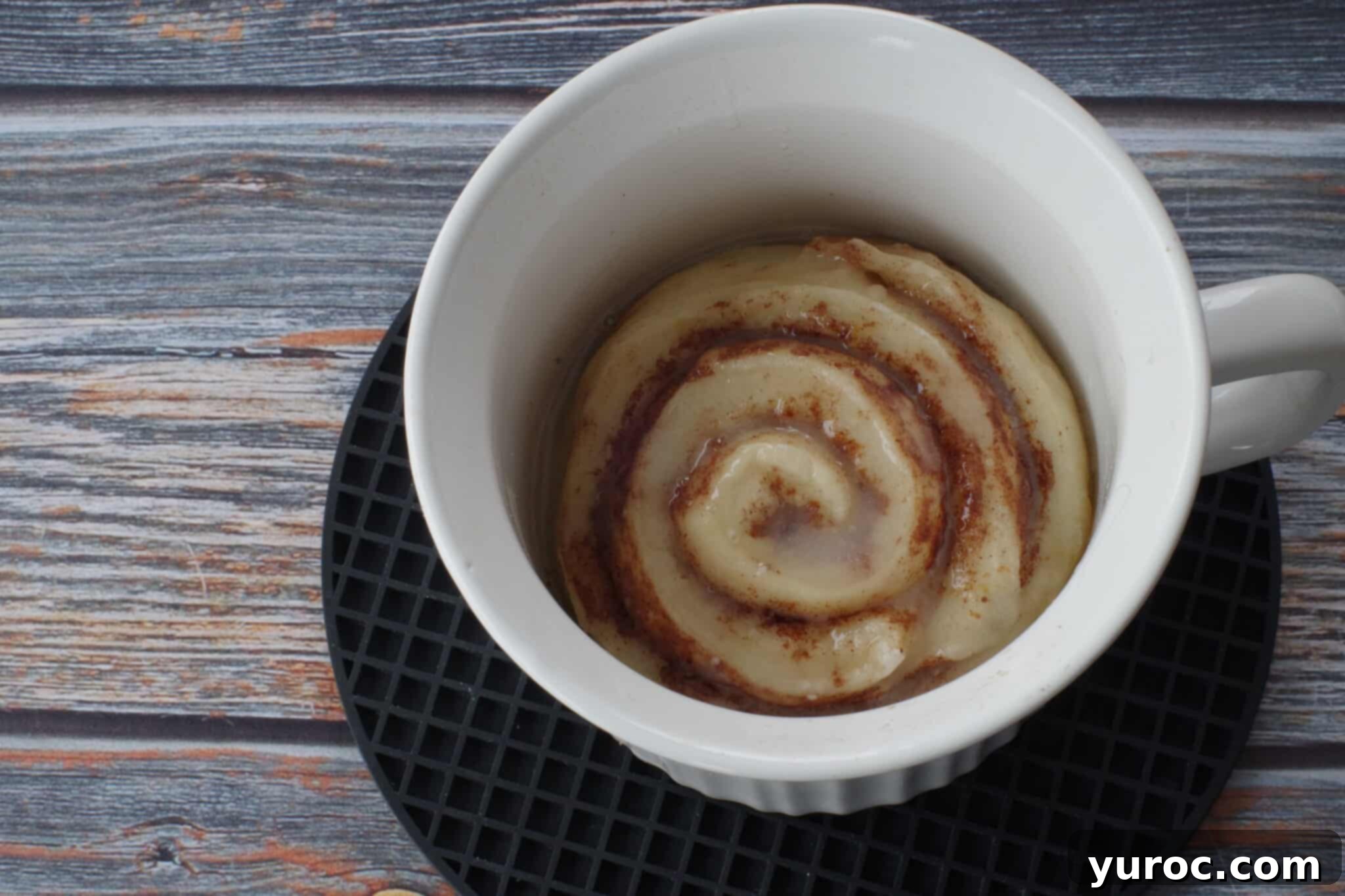 Healthy Cinnamon Swirl Mug Treat 17 glaze poured over warm cinnamon roll in meal mug on black round trivet