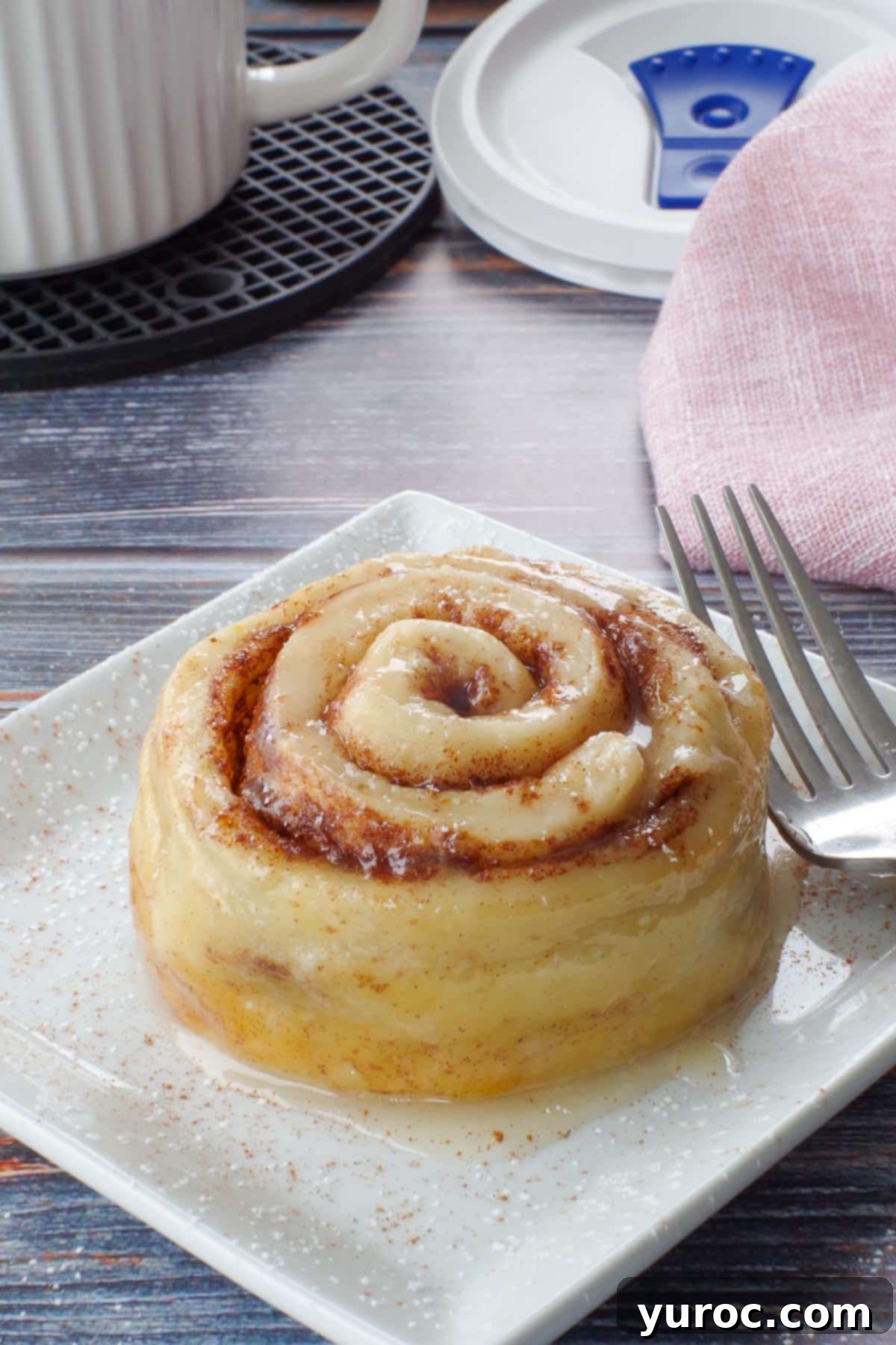 Healthy Cinnamon Swirl Mug Treat 21 cinnamon roll on a white square plate with a fork, and a meal mug and pink napkin in the background