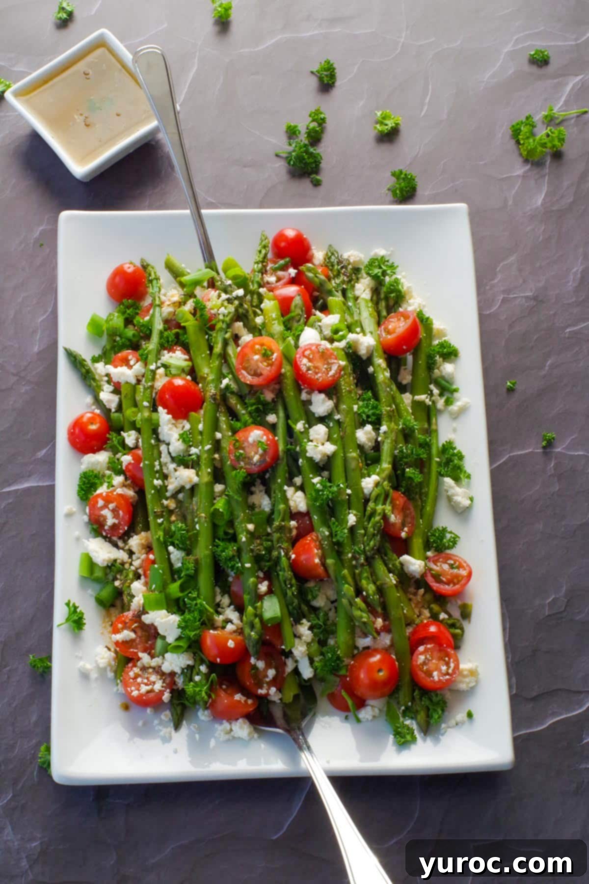 asparagus and tomato salad on a white platter with dressing in the background