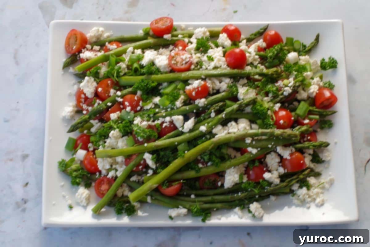 feta cheese and parsley sprinkled on asparagus and tomatoes on white platter