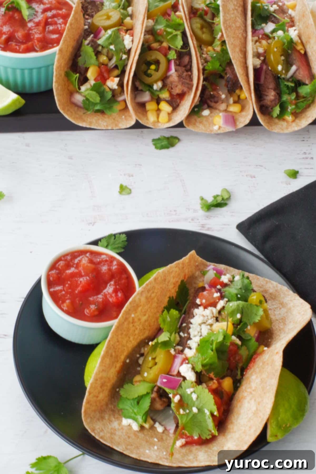 air fryer steak taco on a black plate with salsa, with a tray of more steak tacos in the background