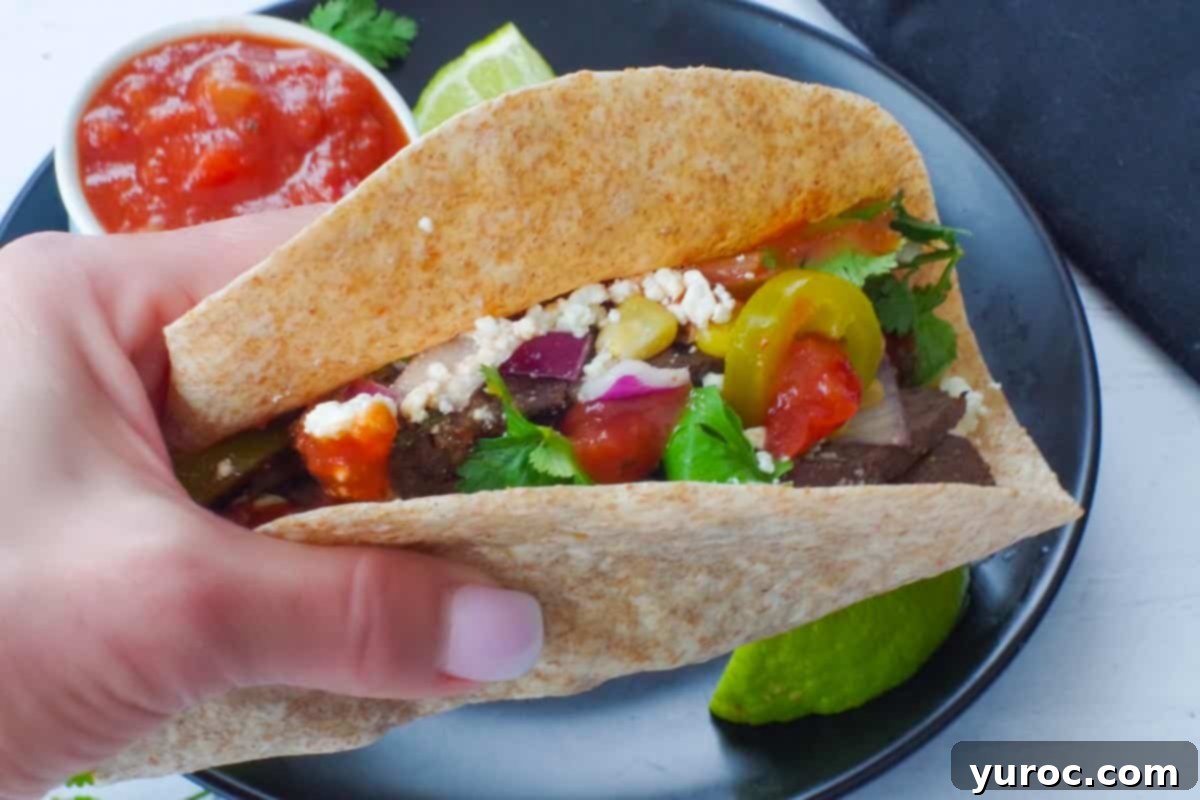 air fryer steak taco held in a hand with a black plate below