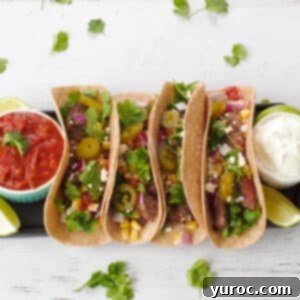 Air fryer steak tacos with a dish of salsa on one side and a dish of sour cream on the other, as well as lime wedges, on a black serving tray