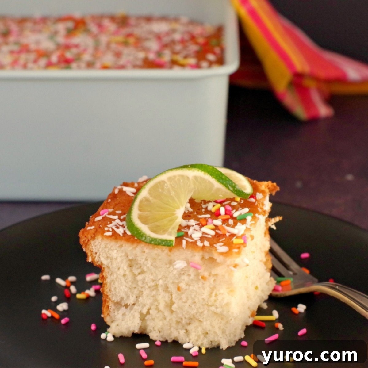 coconut tres leches cake on a black plate with a fork, with a whole cake in the background