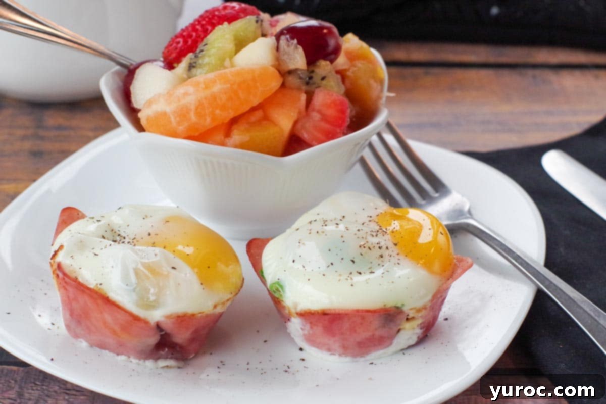 2 healthy eggs benedict on a white plate with a fork and a bowl of fruit