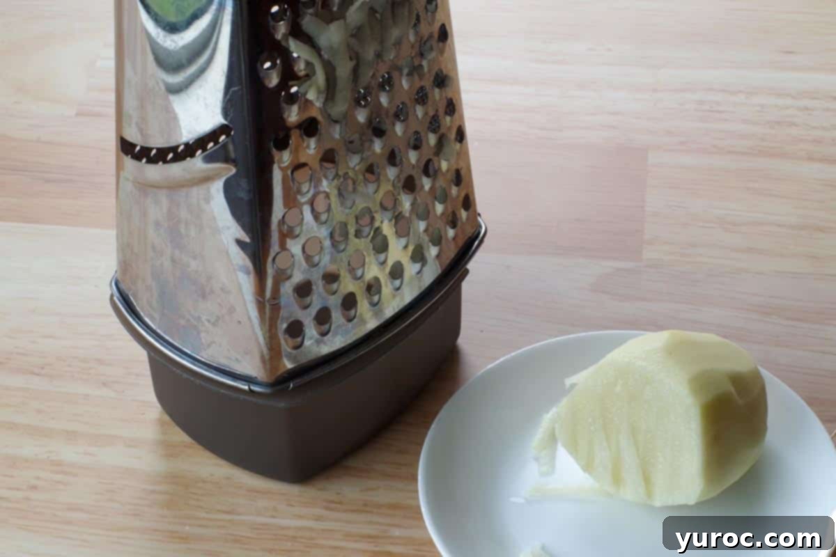 box grater beside ½ a grated potato on a white plate