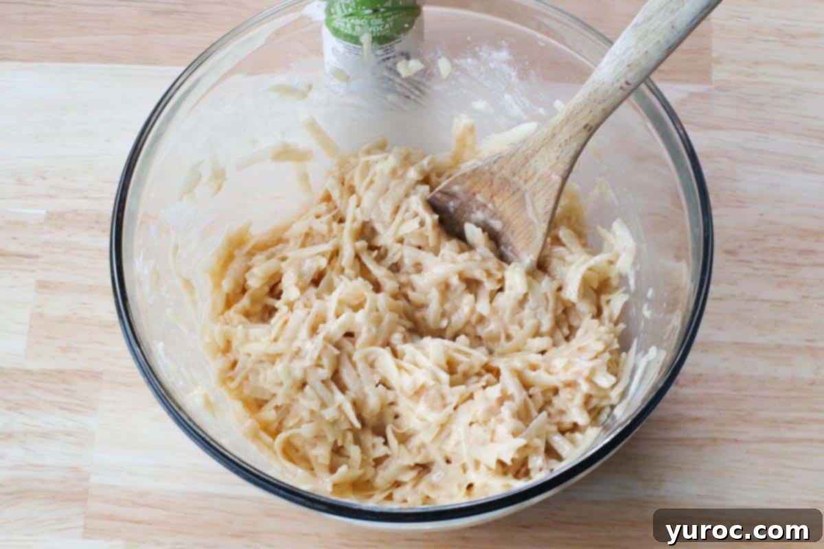 shredded potatoes mixed with other ingredients in a large glass bowl with a wooden spoon