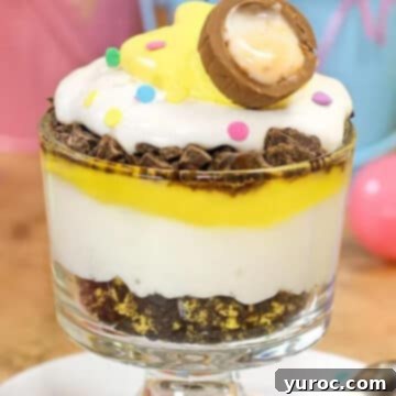 An inviting Easter Trifle, beautifully displayed in a glass trifle dish, with charming Easter decorations subtly arranged in the background.