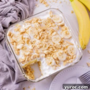 A delightful banana dessert recipe presented in a glass 8x8 pan, with a piece neatly removed. Fresh bananas are visible on one side, complemented by a soft mauve linen on the other.