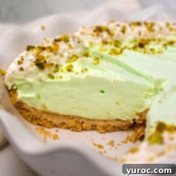 A vibrant pistachio cream pie presented in a white pie dish, with two pieces already enjoyed.