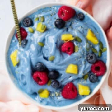A vibrant blue smoothie bowl adorned with fresh fruit and a gleaming gold spoon, perfect for a healthy and colorful treat.