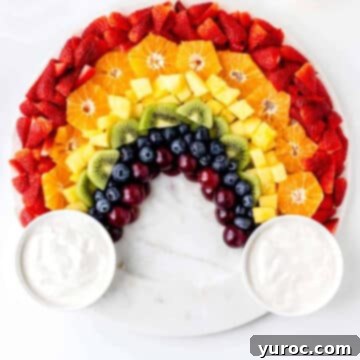 A beautiful rainbow fruit board featuring a variety of fresh, colorful fruits arranged with round bowls of dip on either side.