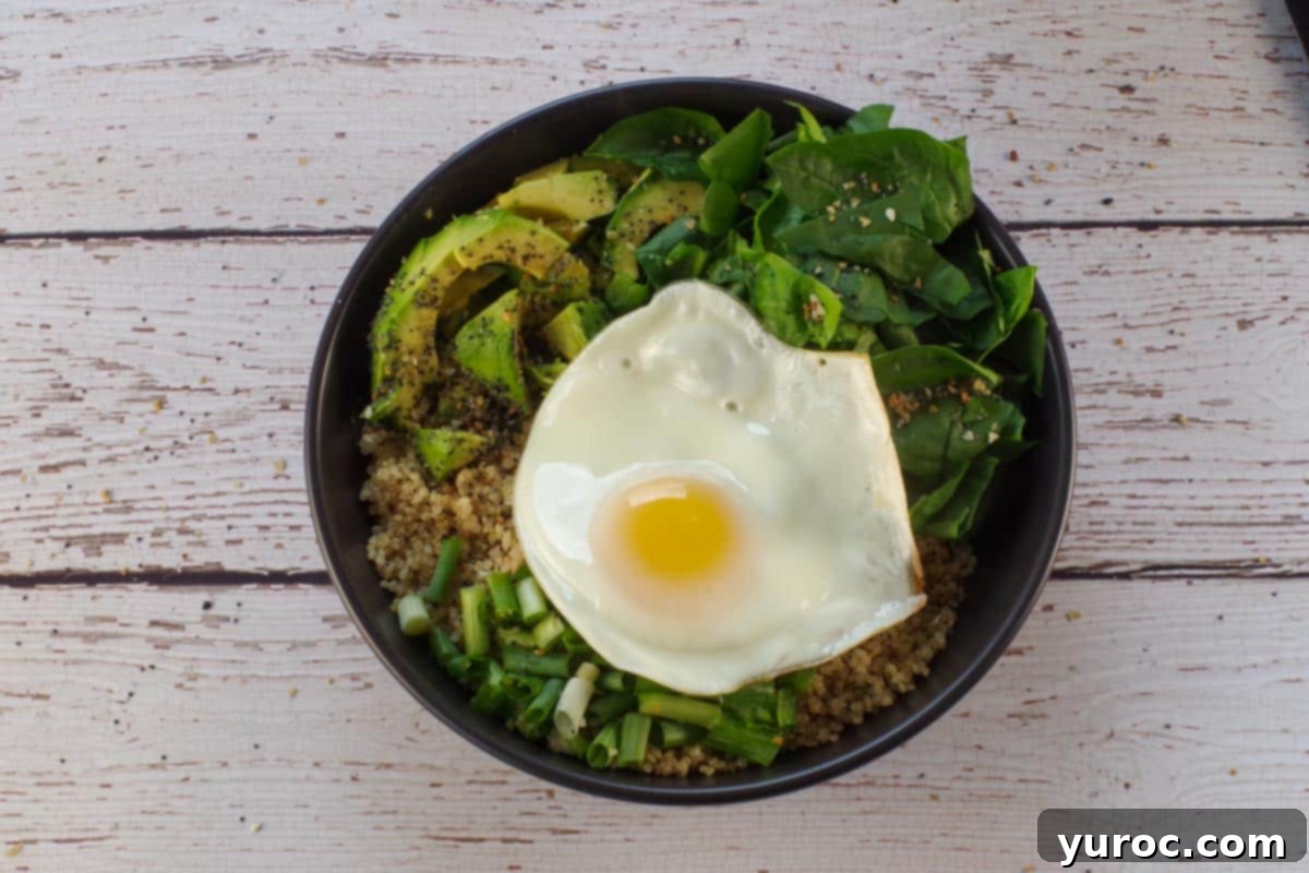 Avocado Breakfast Power Bowl 8 Fried egg placed on top of veggies and quinoa in black bowl